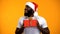 African-American man in Santa hat presenting Christmas gift, yellow background