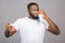 African american man standing over isolated grey background, illness and fever, flu and cold, virus sick, using thermometer