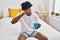 African american man tired drinking cup of coffee sitting on bed at bedroom