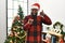 African american man wearing santa claus hat standing by christmas tree smiling doing talking on the telephone gesture and