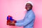 African American man wearing stylish plaid shirt great smile in santa hat with gift box on pink background studio.dark