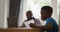African american man working at home using laptop, sitting at table with son doing school work