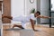 African-American man working out, doing stretching exercise on yoga mat while watching fitness video