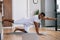 African-American man working out, doing stretching exercise on yoga mat while watching fitness video