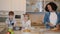 African-American nanny cooking food while kids boy and girl watching tablet and eating in kitchen