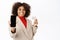 African american saleswoman, corporate woman shows her mobile phone screen and demonstrates credit card, stands over