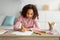 African american schoolgirl sitting at table and drawing, painting with pencils at home, enjoying development activities