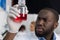 African American Scientist Examine Flask With Red Luquid Working In Modern Laboratory, Male Researcher Making Experiment