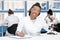 African american scientist in lab coat with clipboard, microscope and digital tablet working in chemical lab