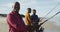 African american senior father and twin teenage sons standing on a beach fishing and talking