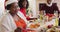 African american senior woman in santa hat serving food in plate while sitting on dining table havin