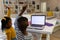 African american siblings raising hands while attending online class over laptop at home, copy space