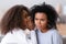 African American teen daughter whispering in unhappy mother ear