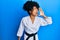 African american woman with afro hair wearing karate kimono and black belt shouting and screaming loud to side with hand on mouth