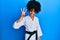African american woman with afro hair wearing karate kimono and black belt showing and pointing up with fingers number three while