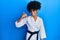 African american woman with afro hair wearing karate kimono and black belt smiling doing phone gesture with hand and fingers like