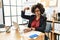 African american woman with afro hair working at the office wearing operator headset strong person showing arm muscle, confident