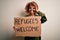 African american woman asking for immigration holding banner with wlecome refugees message with happy face smiling doing ok sign