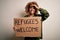 African american woman asking for immigration holding banner with wlecome refugees message stressed with hand on head, shocked