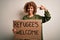 African american woman asking for immigration holding banner with wlecome refugees message with surprise face pointing finger to