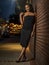 African American woman in black evening dress leaning agasint brick wall