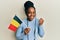 African american woman with braided hair holding belgium flag screaming proud, celebrating victory and success very excited with