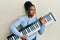 African american woman with braided hair holding piano keyboard clueless and confused expression