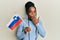 African american woman with braided hair holding slovenia flag covering mouth with hand, shocked and afraid for mistake