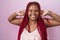 African american woman with braided hair standing over pink background smiling pulling ears with fingers, funny gesture