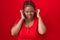 African american woman with braided hair standing over red background covering ears with fingers with annoyed expression for the