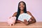 African american woman with braids sitting on the table with piggy bank and dollars looking positive and happy standing and