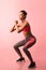 African American Woman Doing Deep Squat On Pink Background