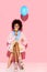 african american woman with flowers in ice cream cone and balloon in hands on pink