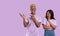 African American woman and her boyfriend feeling shocked, pointing at blank space on lilac background, banner design