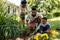 African american woman holding flowers while father and son digging dirt on grassy land in yard