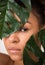 African-american woman looking through green leaves, crop