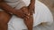 African american woman\\\'s hurting hands touching an injured knee in bed, waking up suffering a painful morning in her bedroom