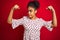 African american woman wearing fashion white dress standing over isolated red background showing arms muscles smiling proud