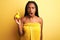 African american woman wearing shower towel holding toy duck over  yellow background scared in shock with a surprise face,