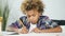 African American young boy is sitting at the dining table and doing school homework.