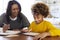 African American  young grandmother sitting at table doing homework with her granddaughter using a tablet computer, close up