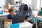 African american young male teacher teaching laptop to caucasian elementary schoolboy at desk