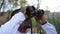 African American young man using binoculars looking away standing in forest on autumn day. Close-up portrait of curios