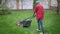 African American young man walking with lawnmower at backyard. Male landscaper gardener using electrical manual