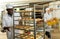 African baker placing tray with formed raw products on trolley