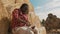 African black farmer sitting on the haystack and holding laptop. Making shade with hand over the face while looking at