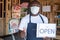 African business owner wearing a face mask and holding an open sign in front of his shop and gives a thumbs up