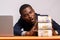 African businessman with a shocked expression holding huge stacks of cash at his desk