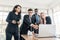 African businessmen standing among Caucasian colleagues looking on laptop at an internal business group meeting.