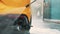 African confident male entrepreneur business suit, washing back of his yellow car manually with water high-pressure hose